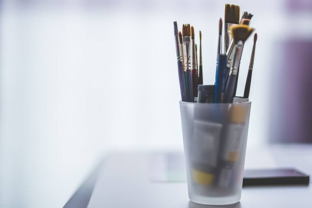 Clear cup with oil painting brushes and paint stored in it