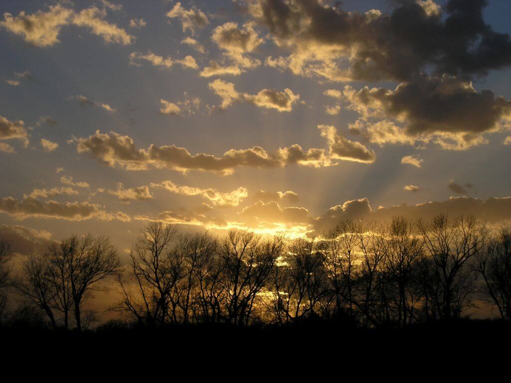 Photograph of sunset streaming through dark clouds