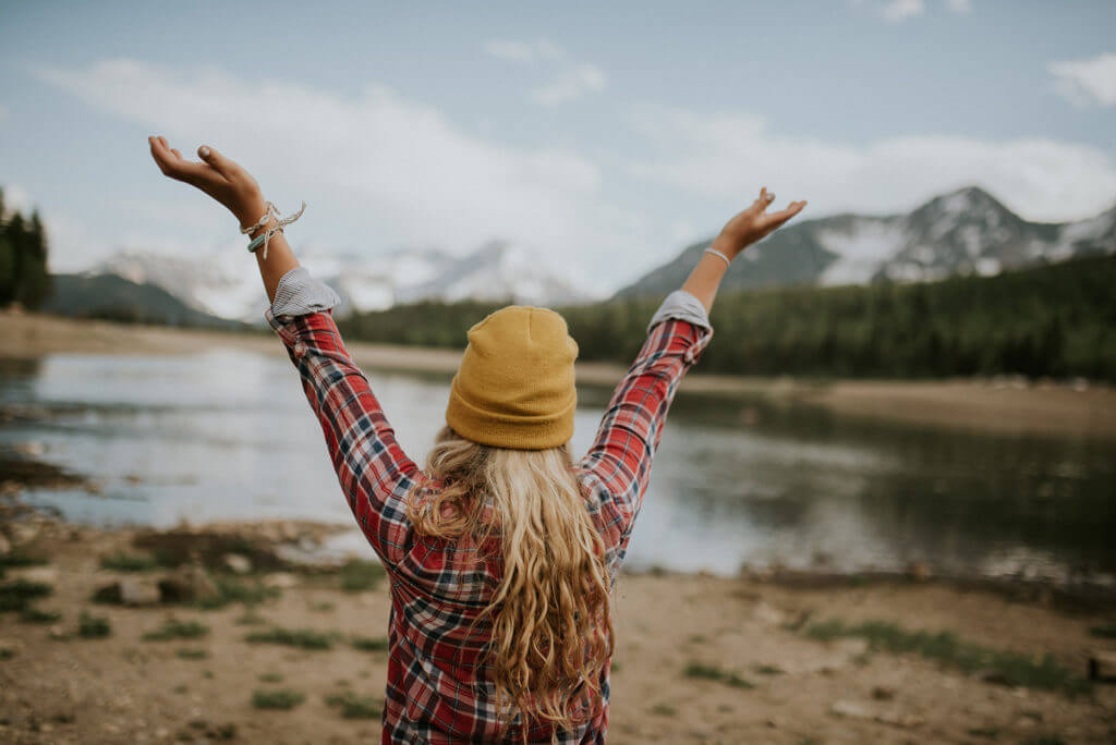 Photograph of woman traveler standing in front of breathtaking lake and mountain scene